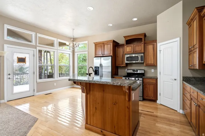 Kitchen featuring wood-finish flooring, wood cabinetry, stainless steel appliances, and a central island with a granite countertop