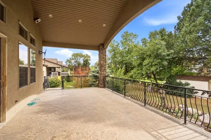 Expansive covered patio with stamped concrete flooring, ornate wrought iron railing, and a stone-clad structural column