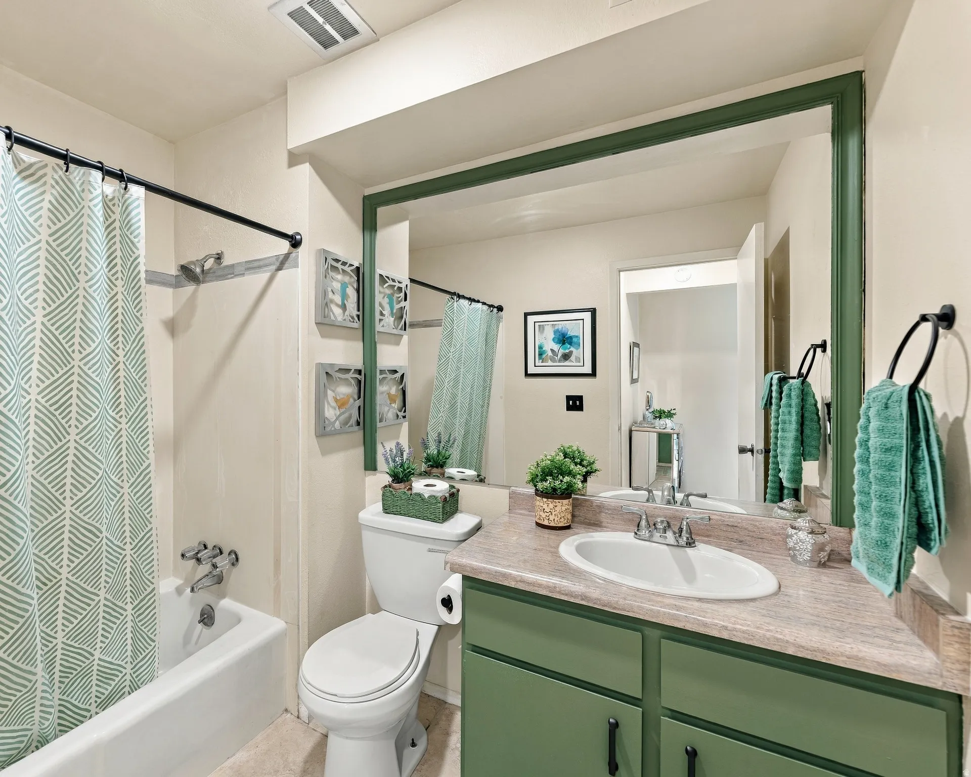 Bathroom featuring a bathtub with shower, vanity with an integrated sink, green-painted cabinetry, and a framed mirror