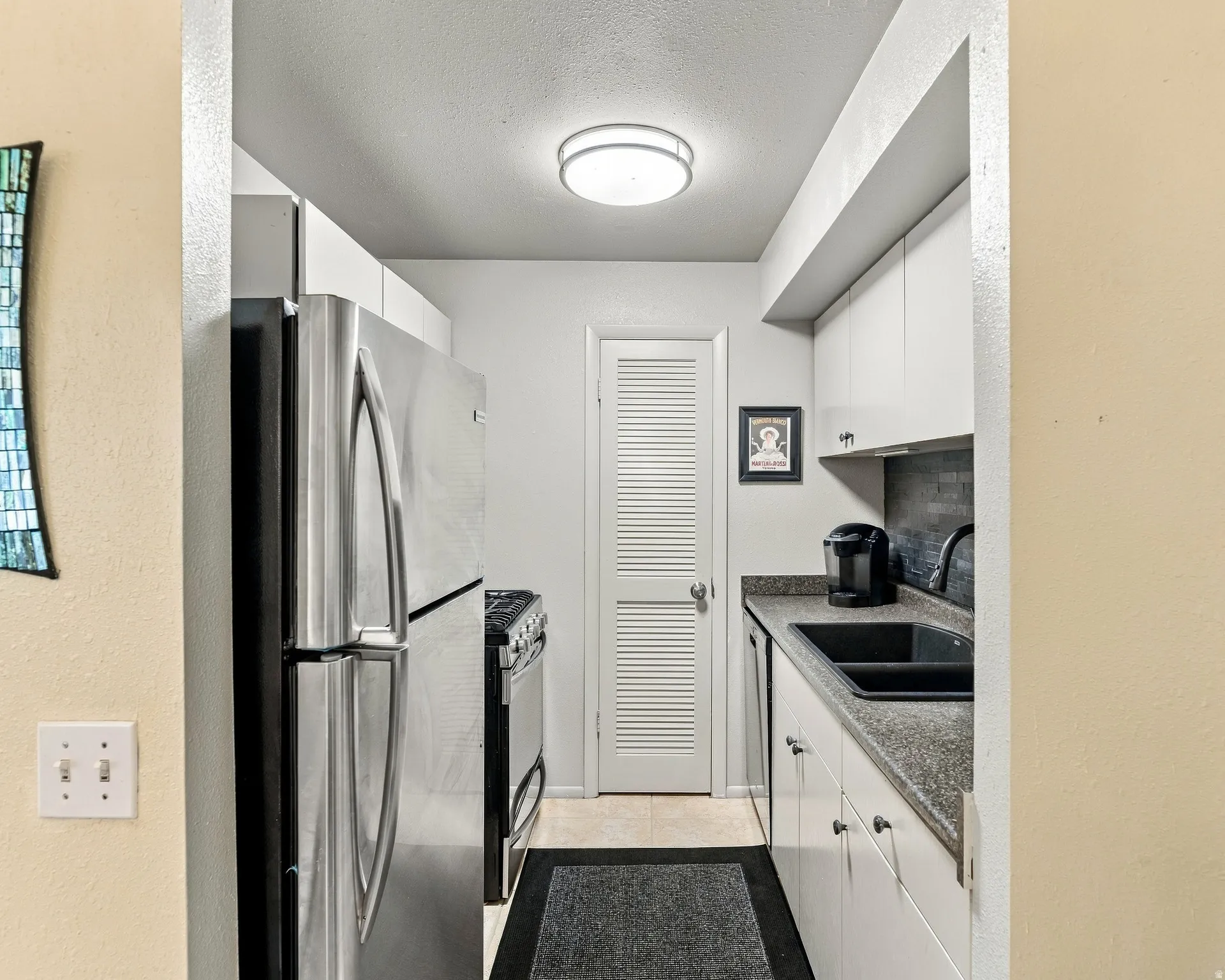 Compact kitchen featuring a stainless steel refrigerator, white cabinetry, dark countertops, and a black sink