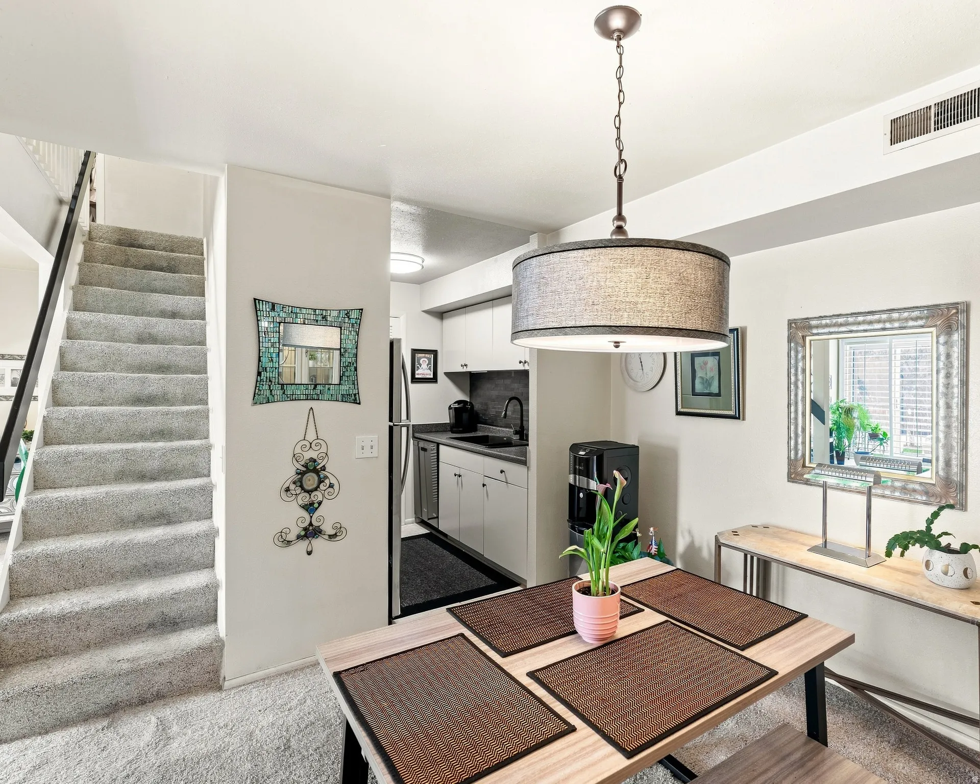 Integrated kitchen and dining area, featuring a contemporary drum pendant light, light-toned wood-finish dining table, and a functional kitchen with light cabinetry
