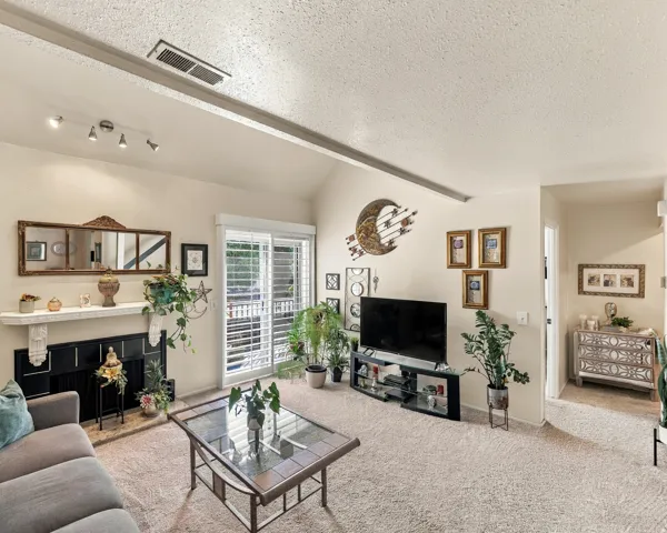 Vaulted ceiling with track lighting, fireplace with a decorative mantel, sliding glass door, and wall-to-wall carpeting