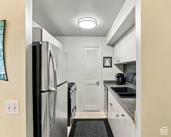 Compact kitchen featuring a stainless steel refrigerator, white cabinetry, dark countertops, and a black sink