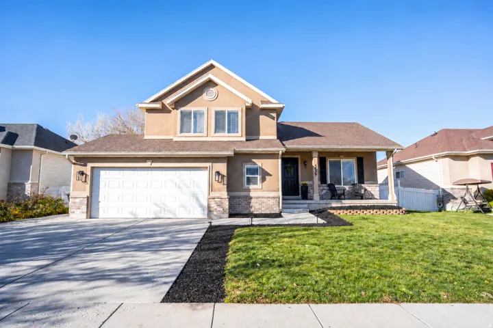 Stucco and stone facade with a two-car garage, covered porch, concrete driveway, and front lawn