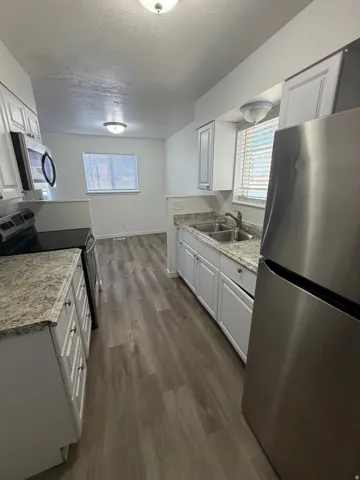 Kitchen featuring wood-finish flooring, white cabinetry, integrated stainless steel appliances, and a double basin sink