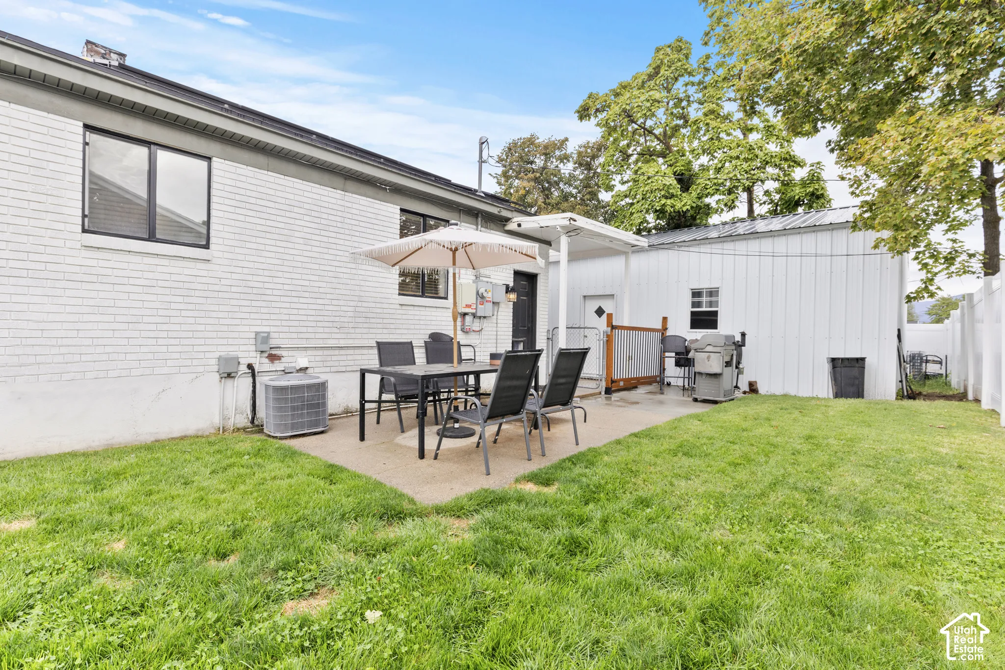 Expansive green lawn with a concrete patio, white brick exterior, and a detached white building with a metal roof