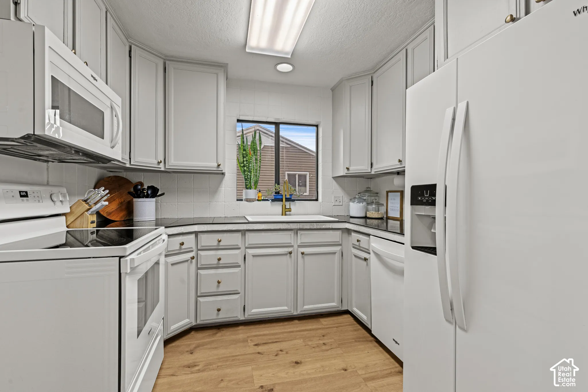 White cabinetry with brass hardware, wood-finish flooring, built-in microwave, and a white tile backsplash