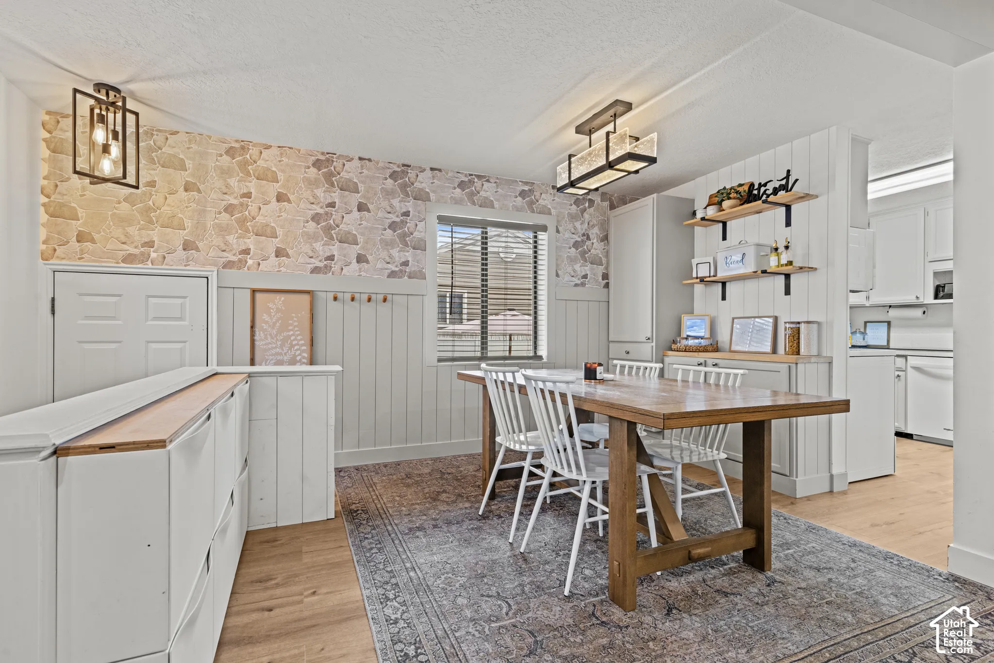 Bright kitchen and dining area featuring white cabinetry, wood-finish dining table, decorative tile backsplash, open shelving with brass hardware, and wood-finish flooring throughout