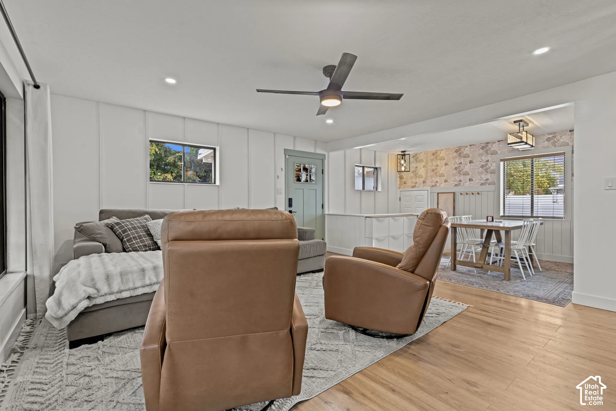 Open-concept living area featuring warm wood-finish flooring, shiplap wall paneling, and abundant natural light