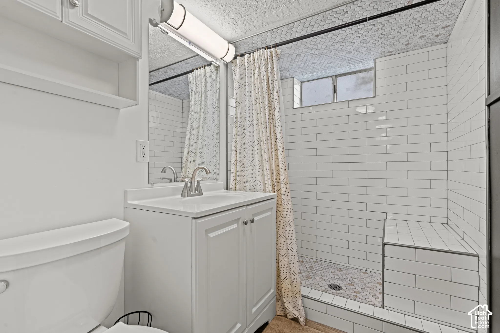 Modern bathroom featuring subway tile surround, a frameless glass shower enclosure with mosaic tile flooring, white vanity cabinetry with integrated sink and brushed nickel faucet, and a white ceramic toilet