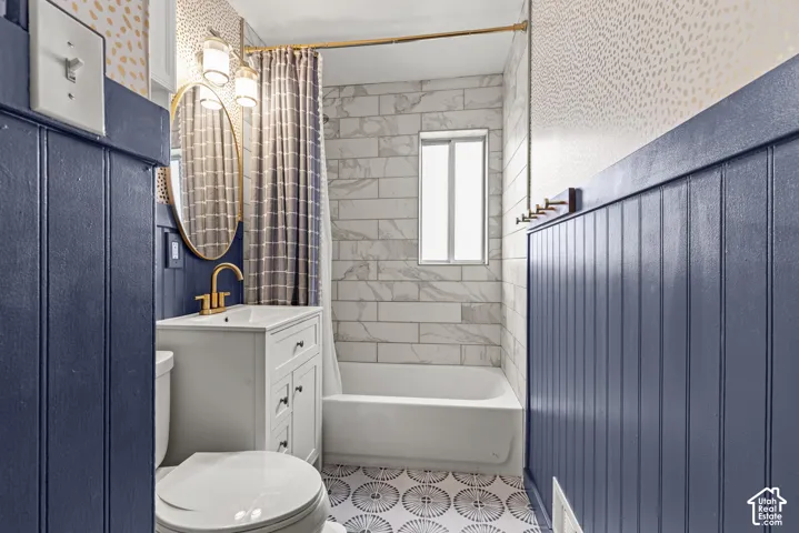 White vanity with gold-finish faucet, subway tile shower surround, window with privacy glass, and decorative floor tiling