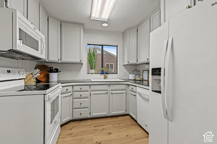 White cabinetry with brass hardware, wood-finish flooring, built-in microwave, and a white tile backsplash