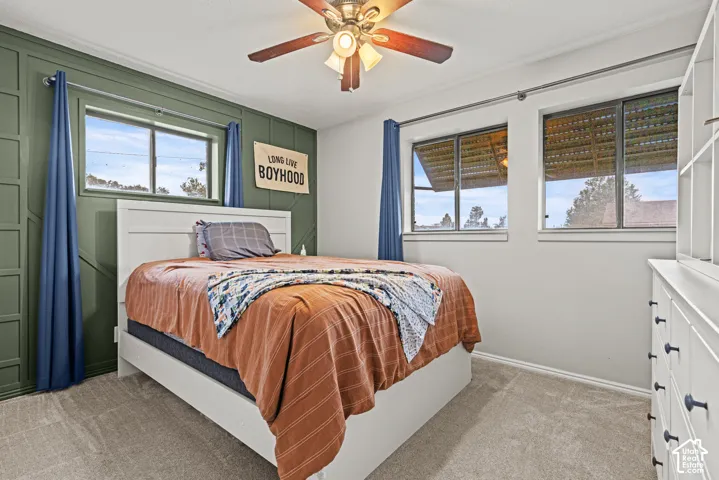 Carpeted room featuring a ceiling fan, multiple windows, a decorative accent wall, and built-in shelving