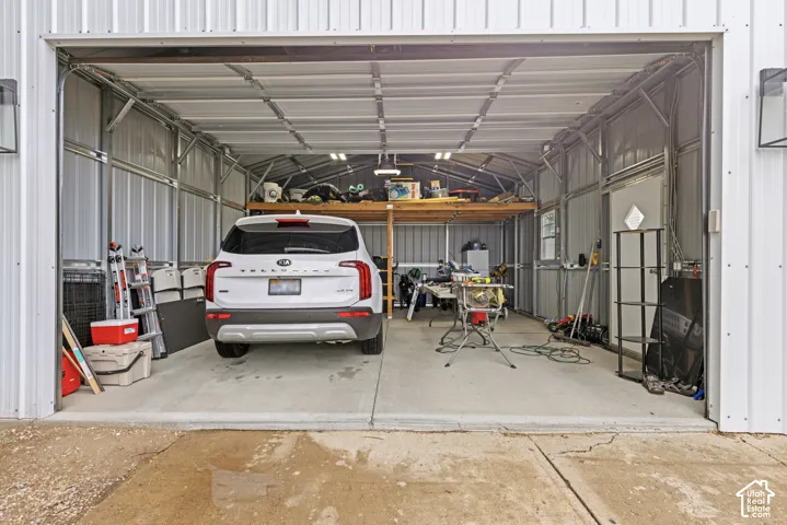 Metal-sided garage structure with an overhead door, concrete flooring, interior shelving, and a built-in loft storage area