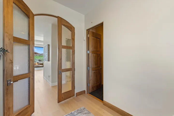Arched doorway with wooden frame and textured glass panels, complemented by light wood-finish flooring and solid wood paneled doors