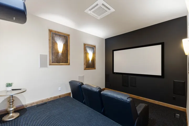 Integrated projection screen, built-in wall speakers, recessed ceiling air register, wall-mounted sconces, and wood-finish trim