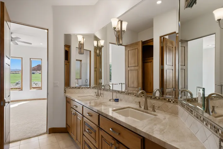 Dual vanity with integrated sinks, stone countertop, wood cabinetry, and extensive mirror
