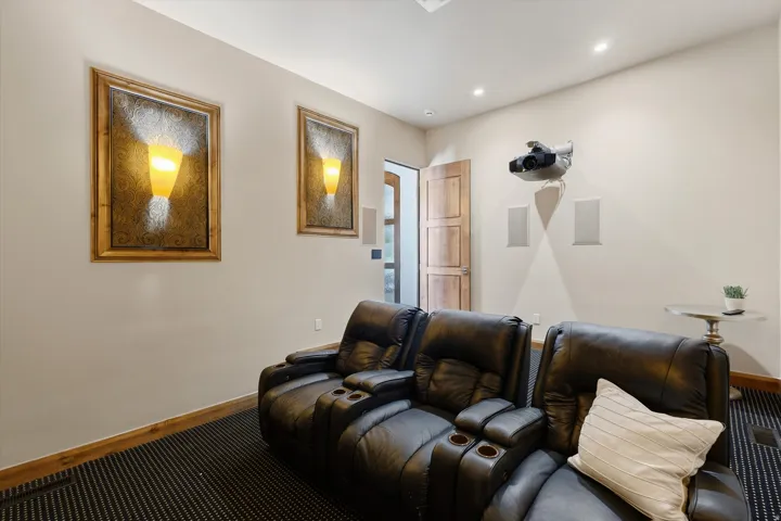 Media room featuring a wall-mounted projector, integrated audio speakers, recessed ceiling lighting, and decorative framed sconces
