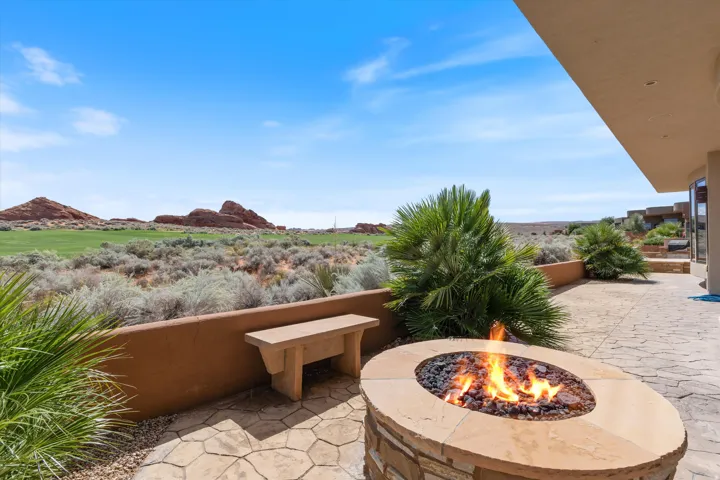 Stone fire pit with a natural gas flame, stone bench seating, concrete patio, and desert landscaping