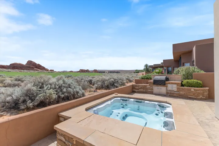 Outdoor spa with stone surround, integrated outdoor kitchen with built-in grill, stone patio, and desert landscape with distant rock formations