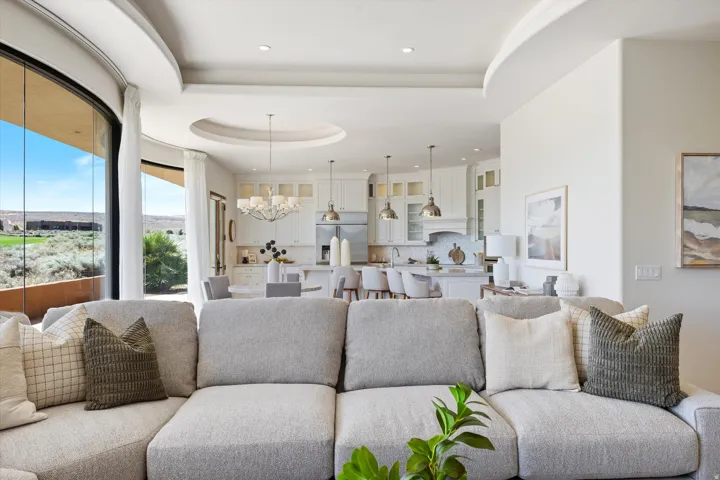Expansive curved window wall, recessed ceiling, open-concept layout, white kitchen cabinetry with glass paneling, and stainless steel appliances