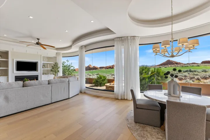 Curved floor-to-ceiling windows, wide plank wood-finish flooring, built-in shelving, fireplace with hearth, and a chandelier