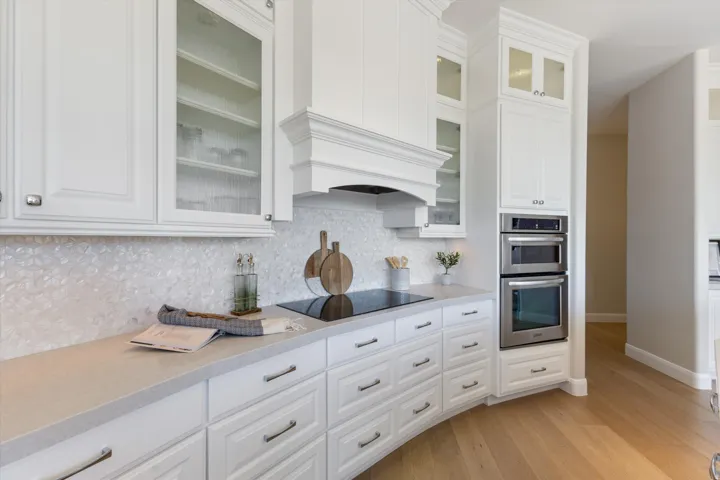 White cabinetry with glass-front display uppers, built-in stainless steel appliances, light-toned countertops, and wood-finish flooring