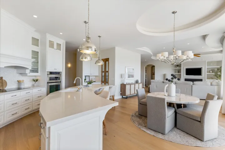 Open-concept kitchen and living area featuring a large curved island with built-in sink, integrated stainless steel appliances, and wood-finish flooring