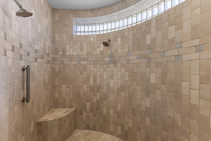 Curved shower enclosure featuring a tiled bench, two shower heads, and an upper glass block window, all within a tiled surround with decorative accent bands