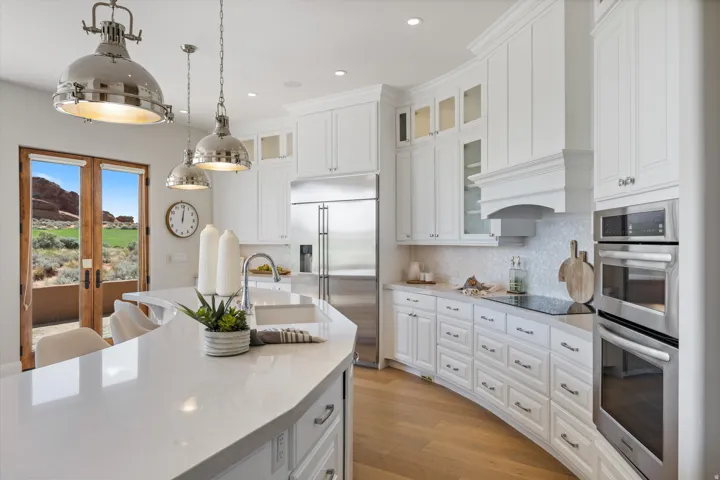 Gourmet kitchen with white cabinetry, stainless steel appliances, and a curved island featuring an integrated sink