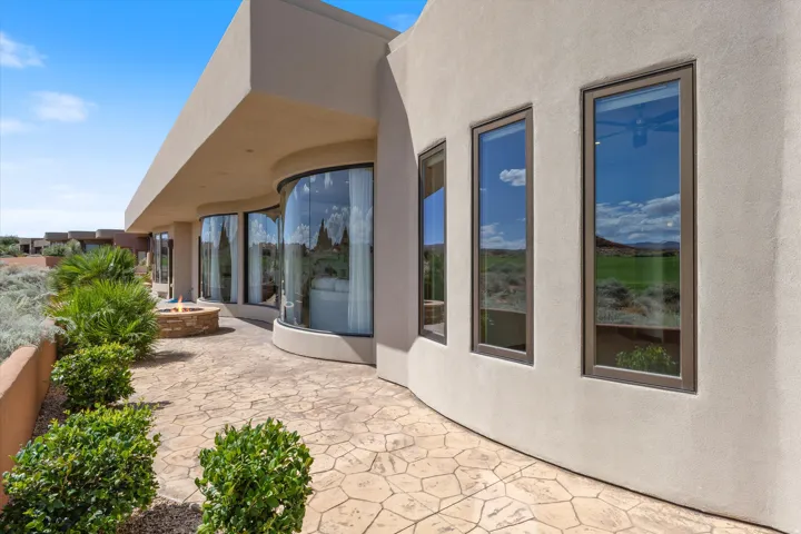 Stucco exterior with a curvilinear wall, stamped concrete patio, built-in fire pit, and curved window wall