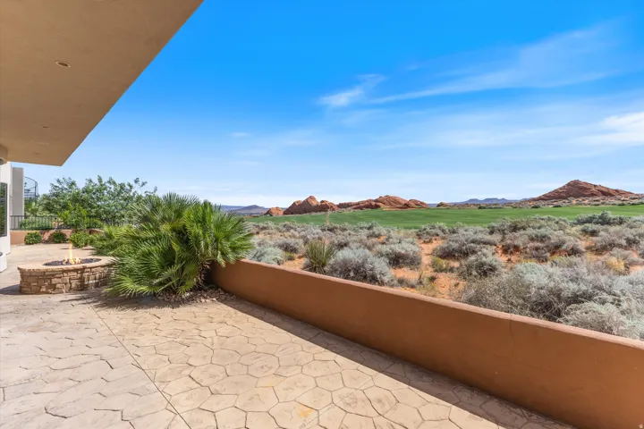 Stamped concrete patio with a stone fire pit, desert landscaping, and a golf course beyond