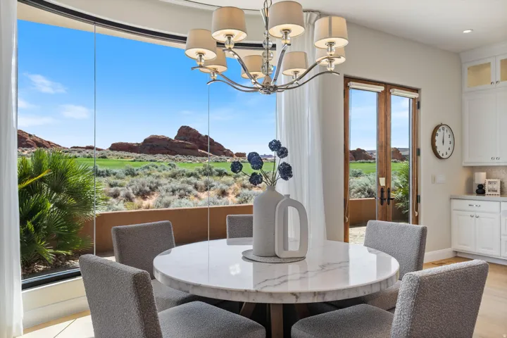Expansive curved window wall, contemporary chandelier, French doors, white cabinetry, and light wood-finish flooring
