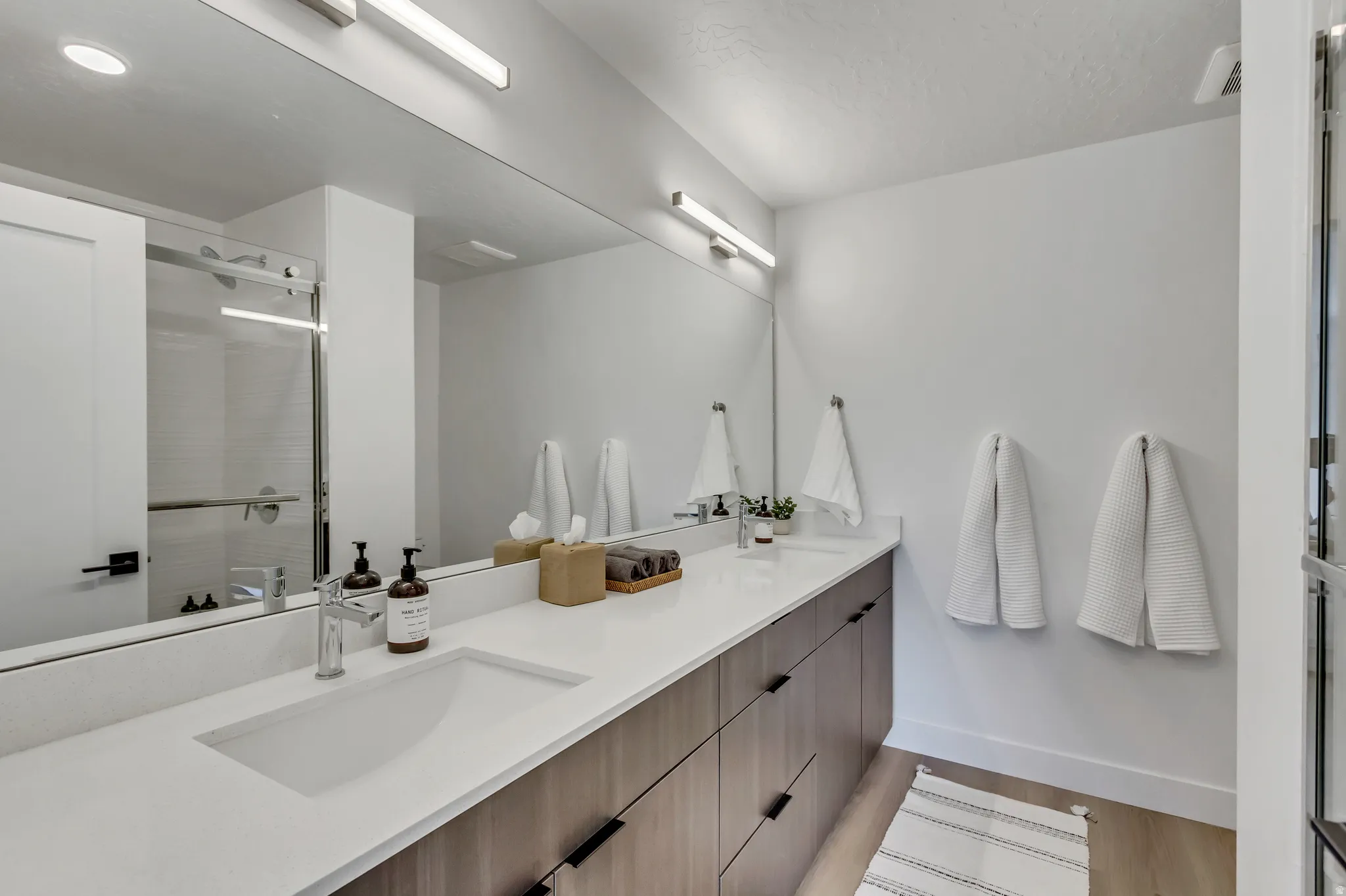 Dual vanity with integrated sinks, ample countertop space, wood-finish cabinetry, and a large mirror with overhead lighting