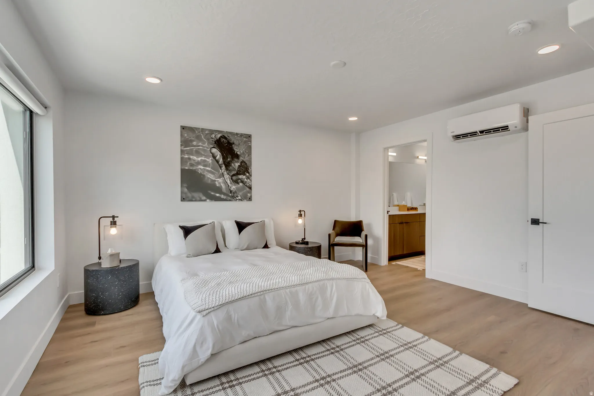 Recessed ceiling lighting, wood-finish flooring, built-in window shade, wall-mounted air conditioning unit, and flat-panel interior door with matte black hardware
