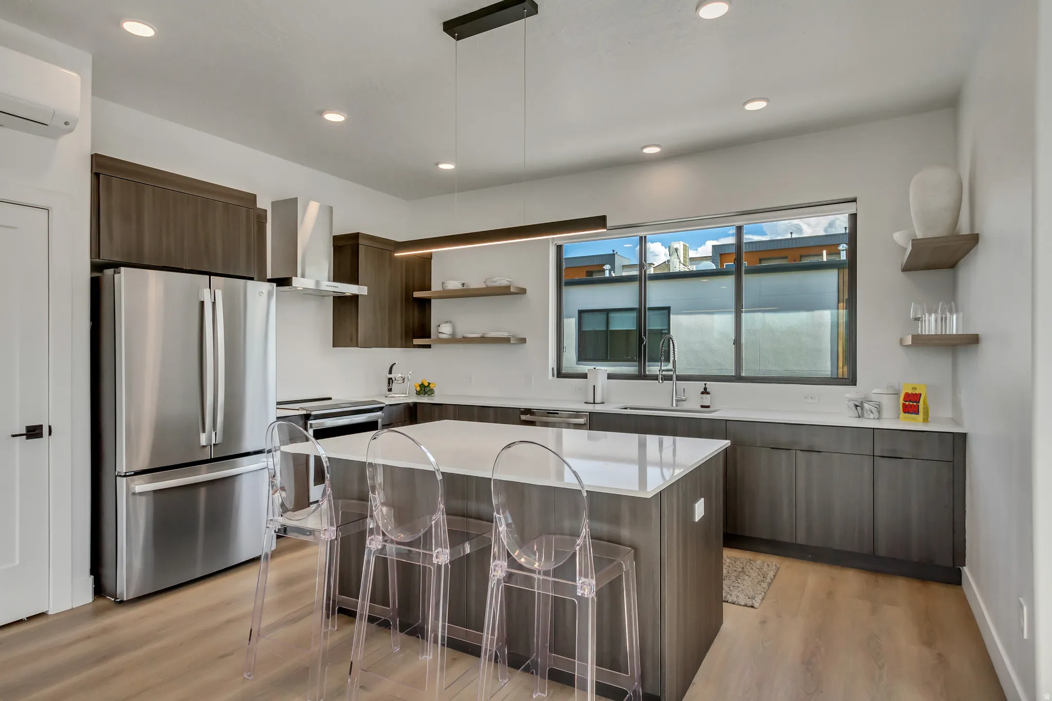 Modern kitchen featuring stainless steel appliances, dark wood-finish cabinetry, a large center island with a light-toned countertop, and recessed lighting
