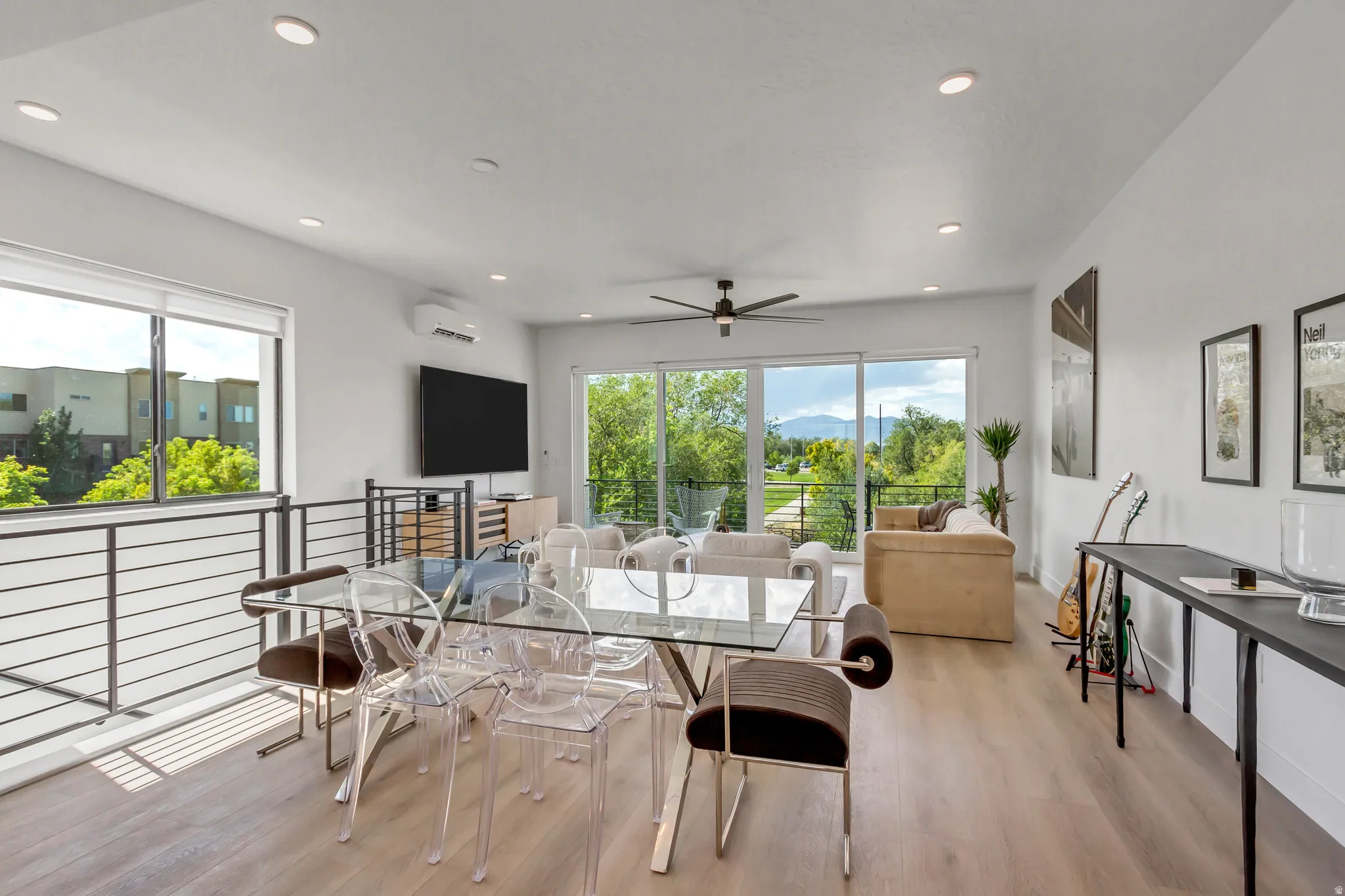 Expansive living area with light wood-finish flooring, a contemporary ceiling fan, recessed lighting, and large sliding glass doors leading to an outdoor balcony