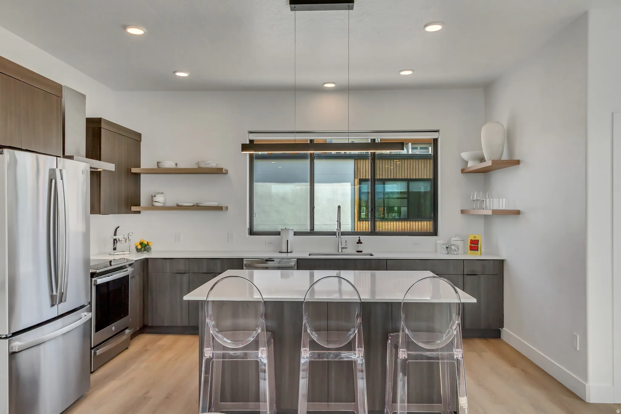 Modern kitchen featuring stainless steel appliances, wood-finish cabinetry, light-toned countertops, a central island, and recessed lighting