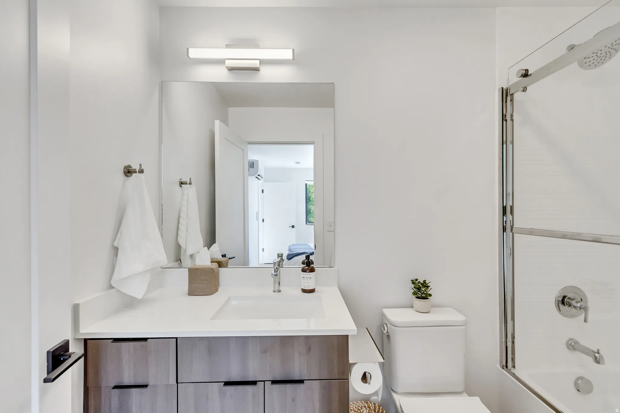 Contemporary bathroom featuring a vanity with wood-finish cabinetry, a white countertop, and a rectangular undermount sink