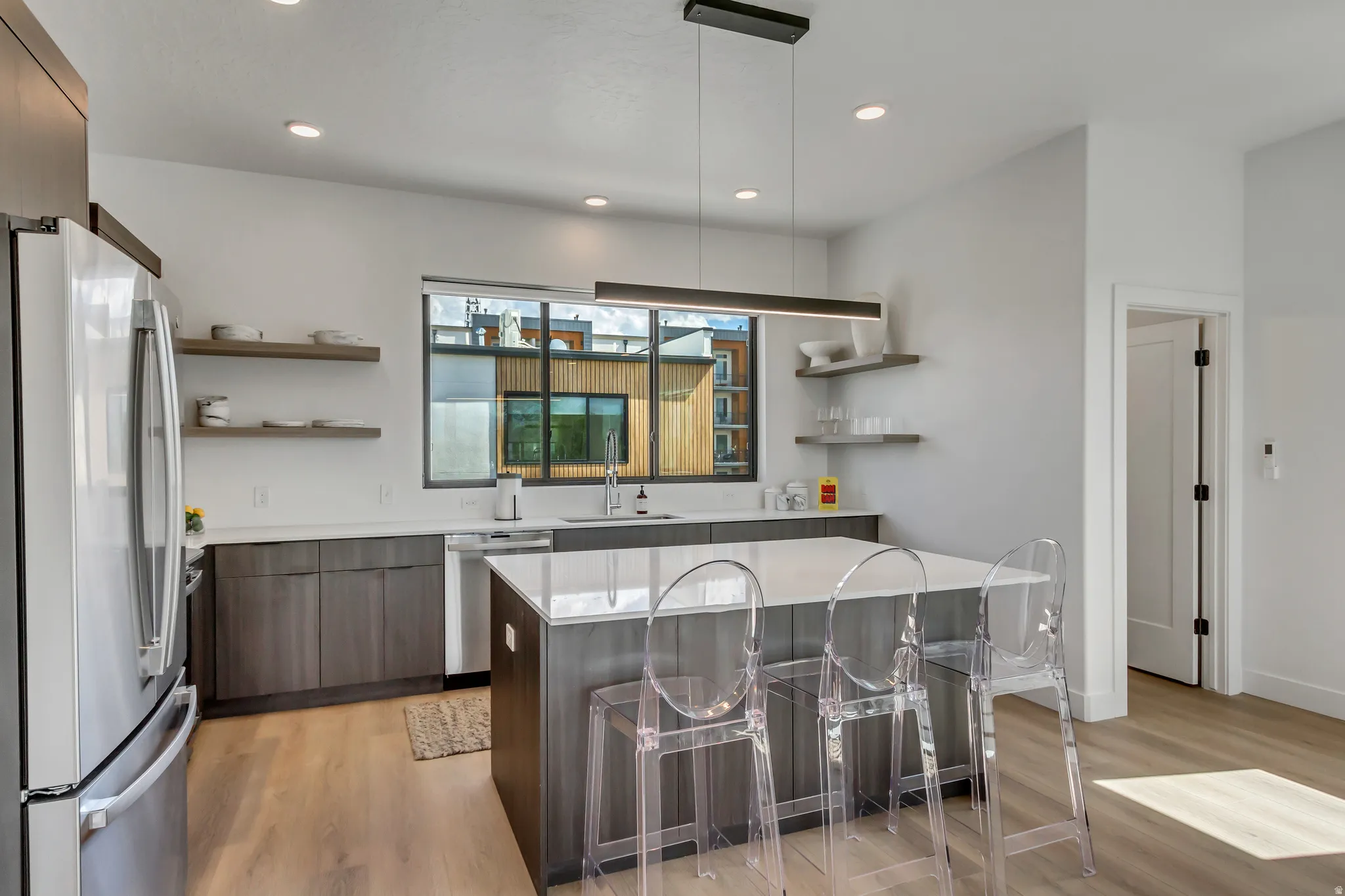 Contemporary kitchen featuring dark wood-finish cabinetry, light stone countertops, stainless steel appliances, a center island with seating, and recessed lighting
