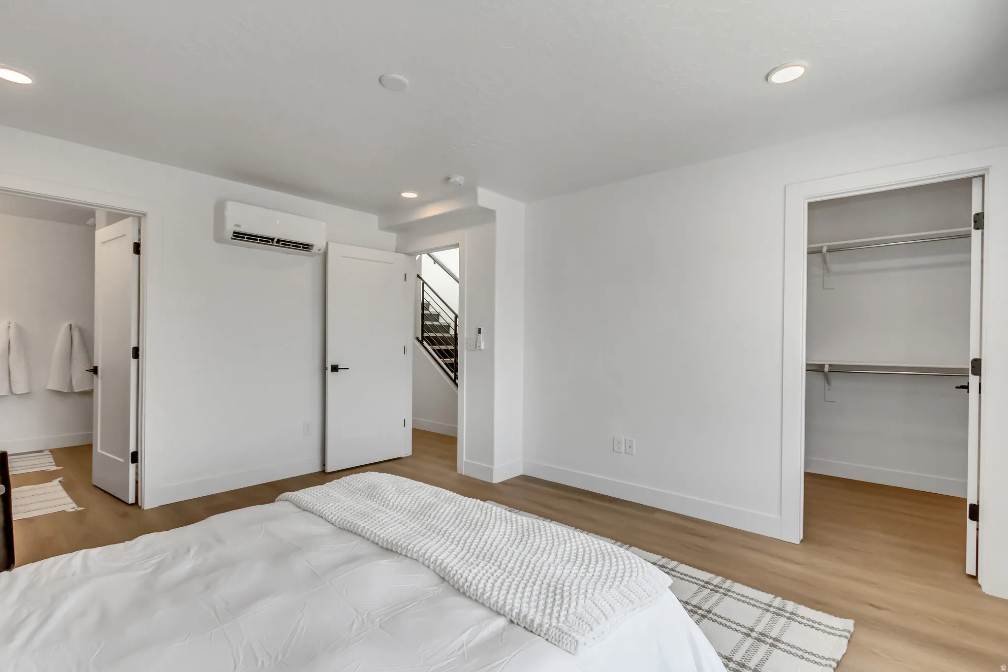 Recessed ceiling lighting, wood-finish flooring, white walls, built-in closet shelving, and a wall-mounted climate control unit
