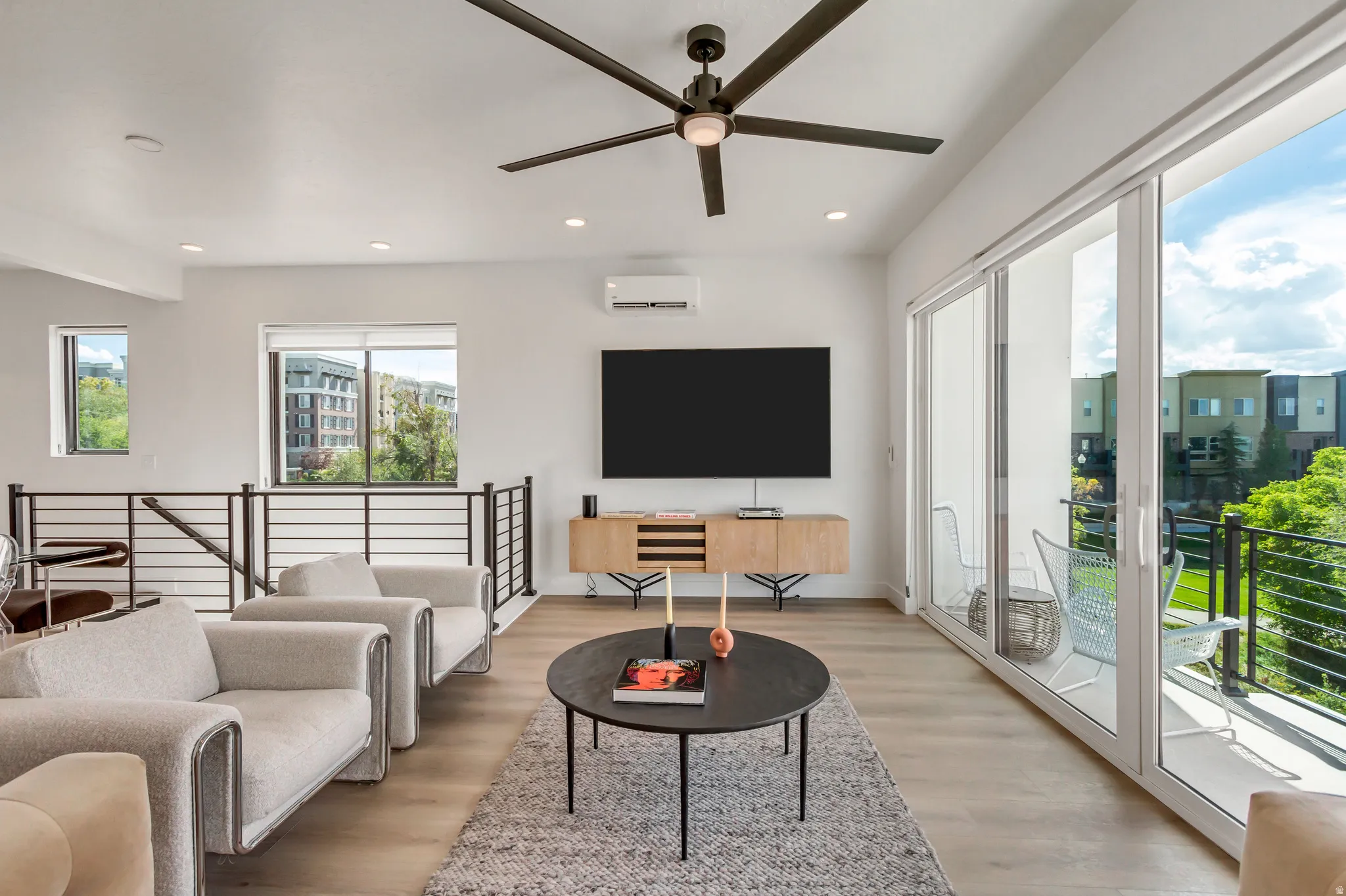 Spacious living area featuring light wood-finish flooring, a contemporary ceiling fan, and sliding glass doors opening to an exterior balcony