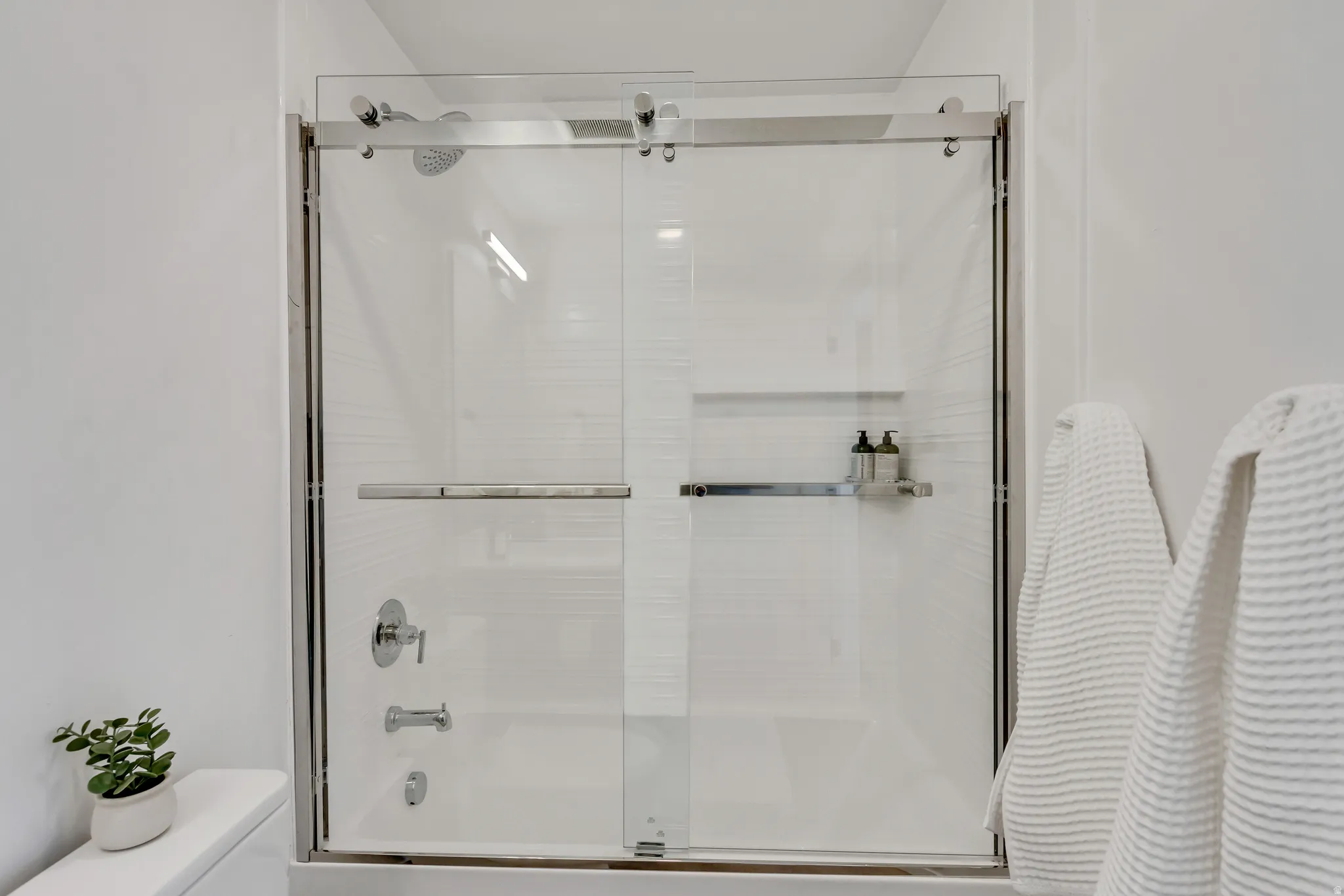 Sliding glass shower enclosure with chrome hardware and integrated showerhead