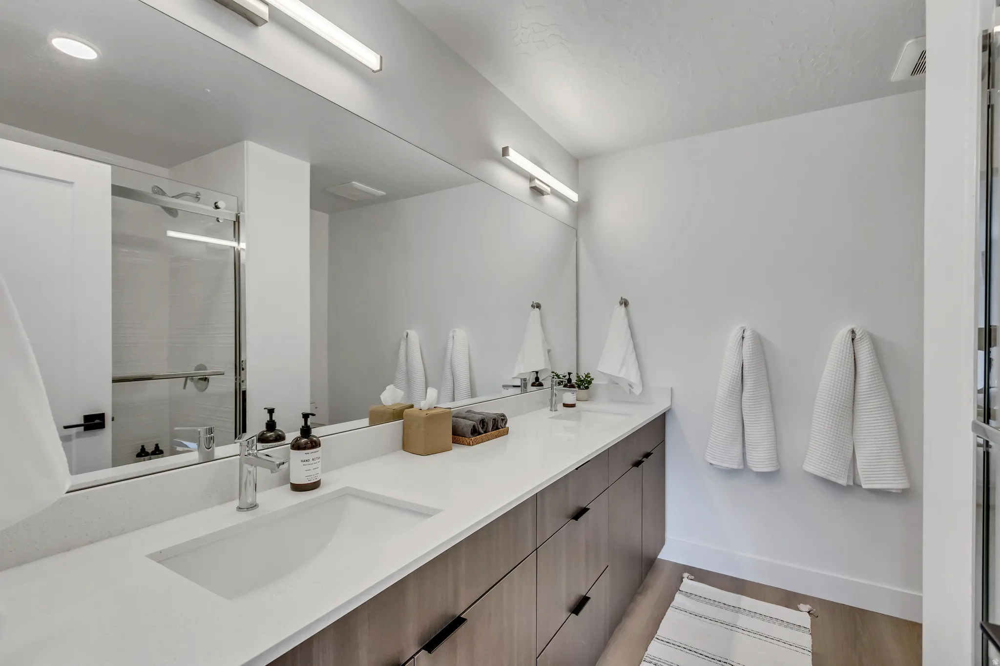 Dual vanity with integrated sinks, wood-finish cabinetry, chrome fixtures, and an expansive wall mirror