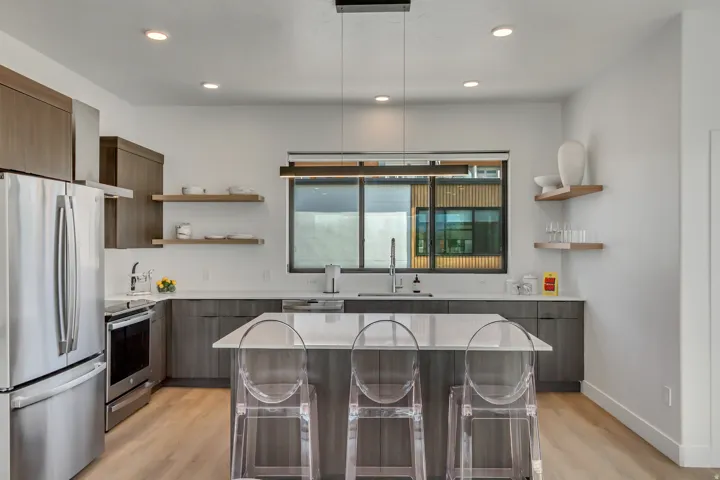 Modern kitchen featuring stainless steel appliances, wood-finish cabinetry, light-toned countertops, a central island, and recessed lighting