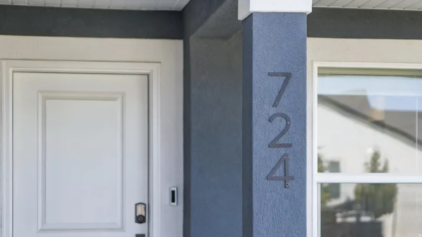 White paneled entry door with smart lock technology, adjacent to a textured column with house numbers