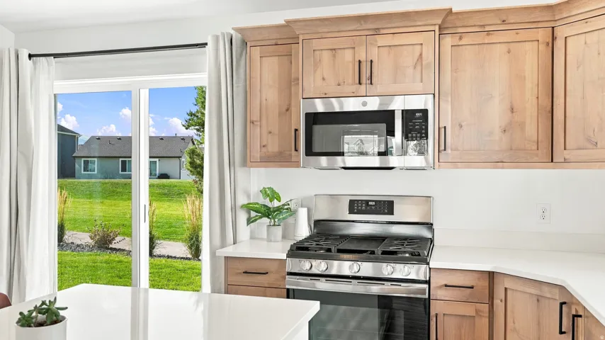 Stainless steel microwave and range, light wood-finish cabinetry with dark hardware, solid surface countertops, and sliding glass doors to the exterior