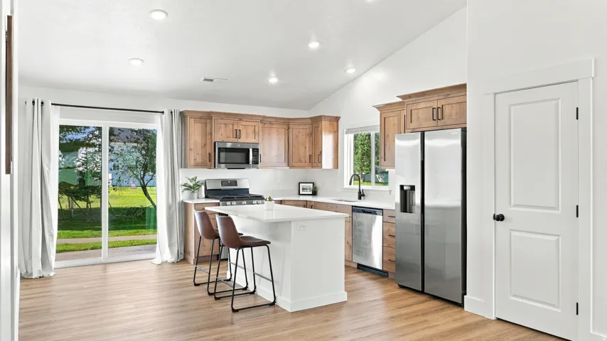 Vaulted ceiling, wood-finish flooring, stainless steel appliances, kitchen island with seating, and sliding glass door