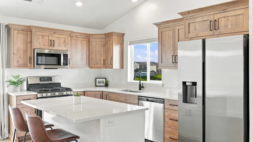 Stainless steel appliances, wood-finish cabinetry, white countertops, kitchen island, and vaulted ceiling