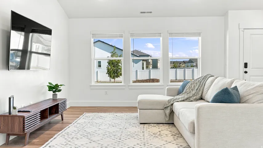 Hardwood-style flooring, white trim, multiple windows, and a wall-mounted television